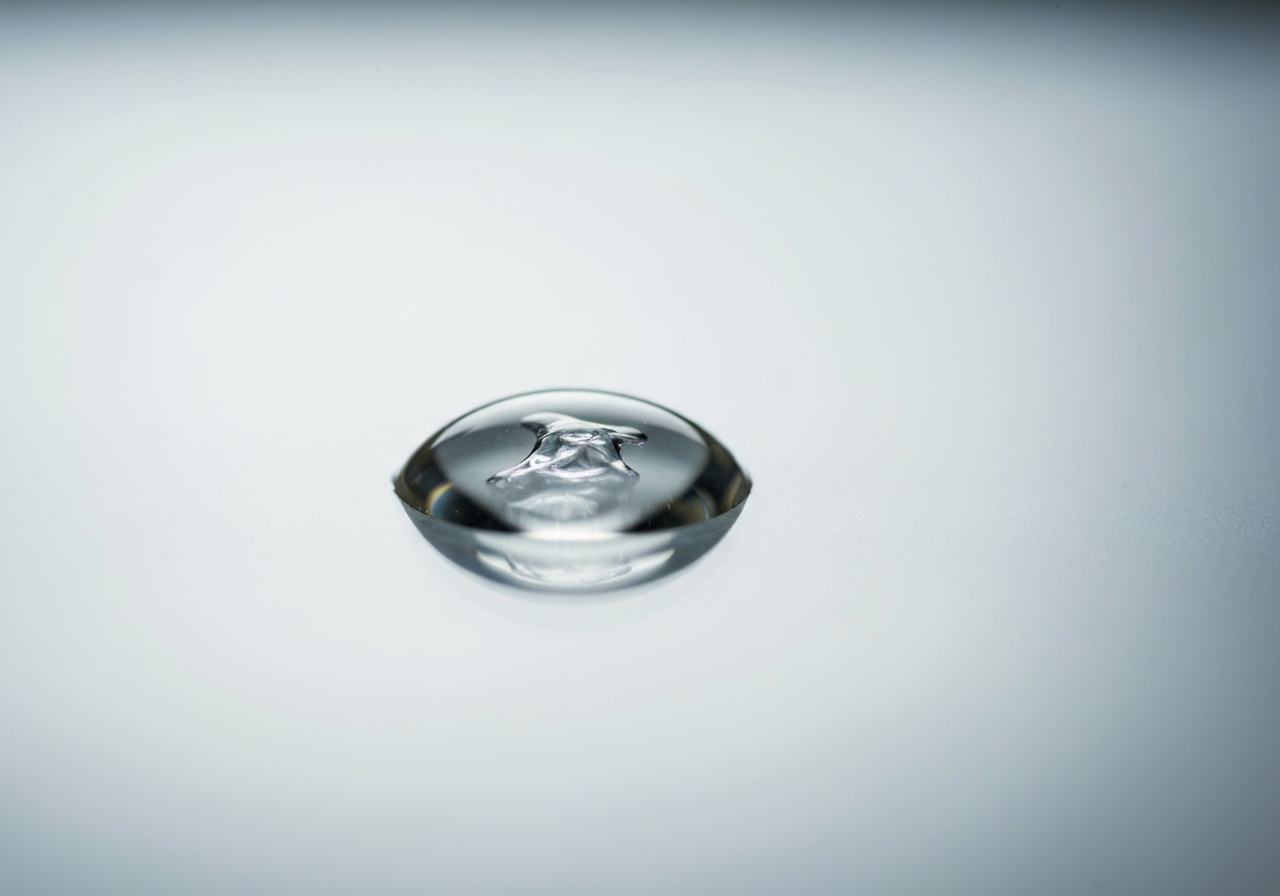 A macro editorial shot of a clear, viscous liquid drop on a glass surface, reflecting soft light, minimalist laboratory background, clean and professional aesthetic, 85mm lens, high detail, no text, no letters